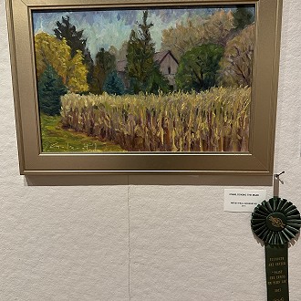 Merit Award: “Over Looking the Maze” by Paul Goderstad. I enjoy the composition of this painting. I like how the corn pulls you into the composition yet has a quiet area of grass that helps your eye move back into the trees and house. The strokes of color add to the impressionistic feel of this painting.