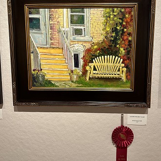 Merit Award: “Clouds Give Way to Sun” by Paula Hare. This painting invites you to enter and sit on the bench for a conversation. The warm color choices drew me in. I enjoy the bold strokes of color and the sunny quality it conveys.  Lovely piece!