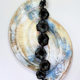 Flower Split                          clay & forged iron                     Artists:  MARK & SYLVIA MONDLOCH          We enjoyed the combination of the asymmetrical design and subtle but intentionally placed color usage on the disk halves used to accentuate the floral element used to visually split the piece. This is an excellent mixed media piece.