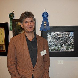 Best of Show- Judges notes: “Homecoming Draped in White” by Troy Tatlock immediately caught my eye. It is a well-executed painting of a subject matter that would normally be considered an eye sore. I kept coming back to the painting and felt a tinge of nostalgia. It seemed possible to step inside the painting and be transferred to a brisk, sunshiny fall day of my senior year of high school. There is a wonderful sense of movement and the slightly off kilter composition is like a nonchalant side glance at the everyday.